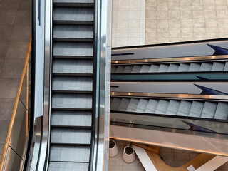Escalators inside a contemporary shopping center viewed from above. Movement, symmetry, and urban architecture symbolizing daily routine and structure.