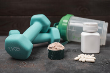Scoop of whey protein powder with white amino acid capsules, fitness dumbbells and shaker bottle on...