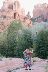Blonde woman poses with hat and sundress with Cathedral Rock in background in Sedona Arizona