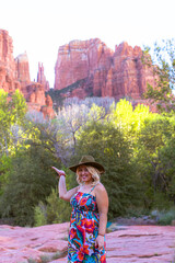 Cute woman wearing a hat and trendy sundress poses at Crescent Moon Ranch in Sedona with Cathedral Rock
