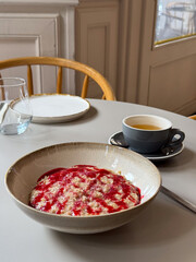 Oatmeal with raspberry sauce and cup of tea on a table. Balanced breakfast, warmth and comfort of cafe life.