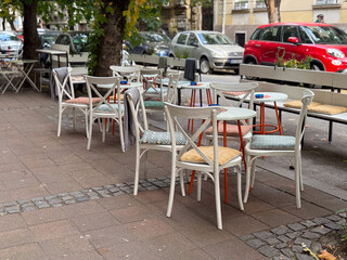 An outdoor cafe terrace with colorful chairs and empty tables on a quiet city street. Urban lifestyle, leisure, and everyday simplicity in a relaxed social environment.