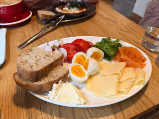 Morning meal with boiled eggs, bread, greens, cheese, salmon, and tomatoes served on white plate. Balanced breakfast representing nutrition and freshness.