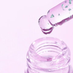 Close-up of dropper with pink skincare serum on pastel pink background with glitter particles.
