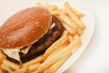 Hamburger with meat and vegetables and French fries. Fast food. Hamburger on a plate.