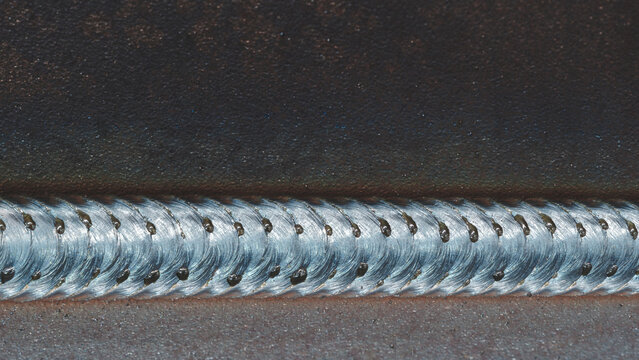 Close-up of metal part with weld seam, the part lies on metal production table in factory or telloconstruction plant as industrial metal concept background.