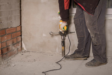 Worker uses electric jackhammer to break concrete at a construction site in the morning sunlight