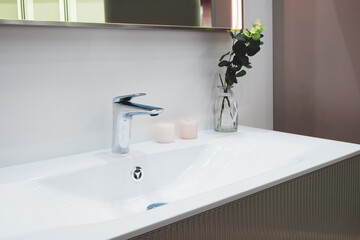 Interior of a bright bathroom with a white ceramic sink, modern faucet, and mirror