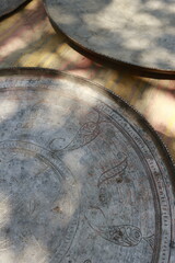 Antique copper trays and dishes with detailed engraving displayed at a flea market in Tbilisi. Warm sunlight and soft shadows create a cozy, authentic atmosphere.
