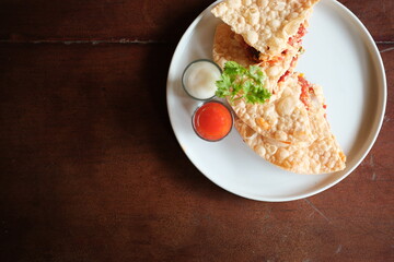 Crispy delicious Indonesian food Kerupuk served with spicy sauce and creamy dip on white plate against dark wooden table, perfect for food blog or cookbook