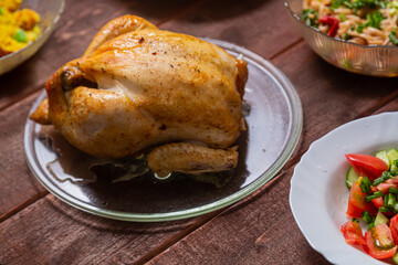Grilled whole chicken on a glass plate on a wooden table