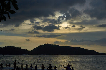 PHUKET, THAILAND - 10 NOVEMBER 2017: Tropical beach sunset with silhouetted people and cloudy sky over calm ocean waters.