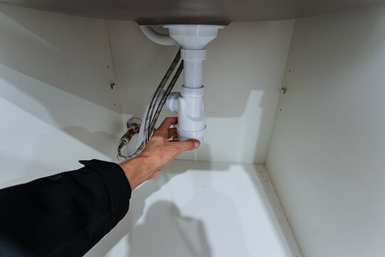 plumbing repair process, accessing plumbing trap for cleaning and maintenance, illustration of hand reaching underneath sink to maintain and inspect drain components properly