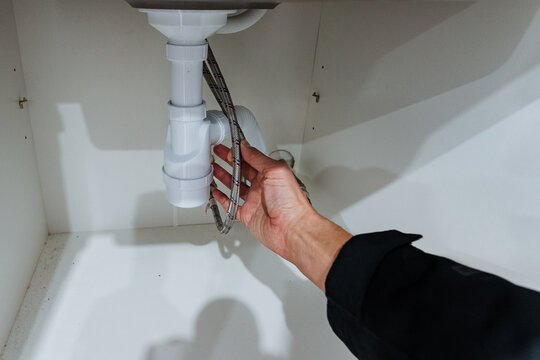 hand adjusting mounting bracket and hoses beneath sink, detailed maintenance gesture with visible fittings and cabinet base, staged for professional service or howto content