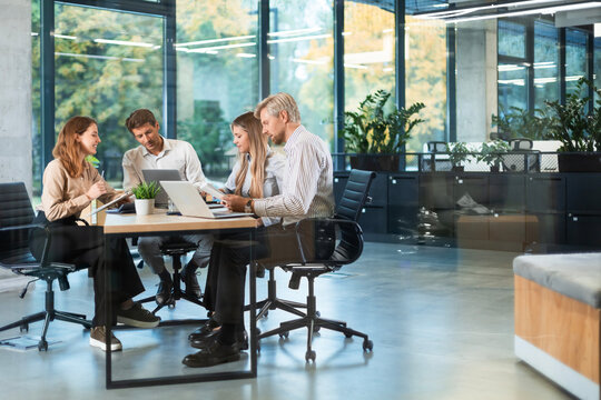 A view through a glass partition shows a modern, busy office interior. Business people are working at desk