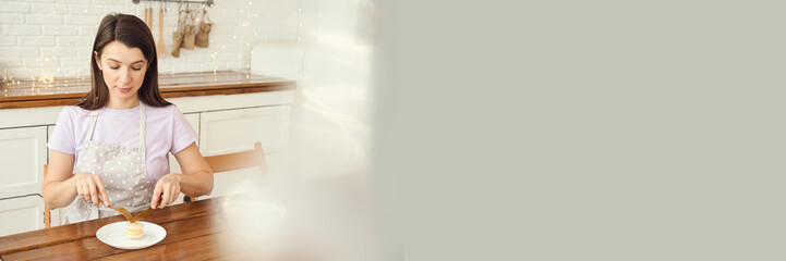 Young caucasian female enjoying pancakes in cozy bright kitchen setting with wooden counter and string lights.