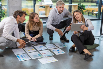 Business people looking at project plan laid out on floor, discussing new project plan in modern office.