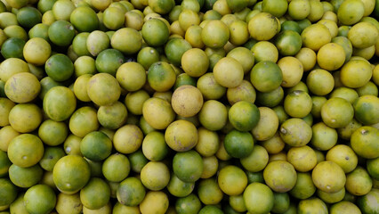 Mix of fresh green and yellow lemons displayed in large heaps at traditional vegetable market showing color and freshness