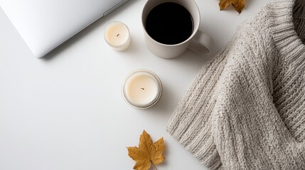Minimalist flat lay: Knitwear, coffee, laptop, notebook, scattered autumn elements, candles on white. Copy space.