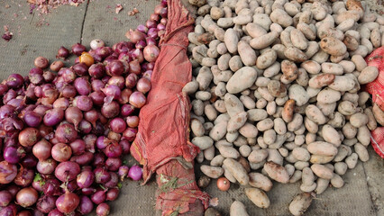 Traditional vegetable market with separate heaps of fresh potatoes and onions placed on ground...