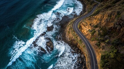 Aerial view of a winding coastal road hugging a cliffside, with crashing waves below