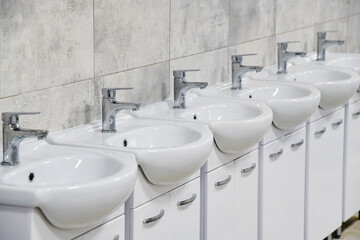 Several new and clean sinks with the same shiny chrome faucets are lined up in a row.