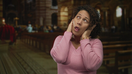Woman presses fingertips into ears inside a catholic church aisle with wooden pews and stained glass windows; frustration isolation disconnection.