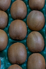 Close-up view of ripe kiwis arranged in a green tray. The image captures their brown fuzzy skin and natural texture, ideal for concepts of freshness, vitamins, and healthy eating.