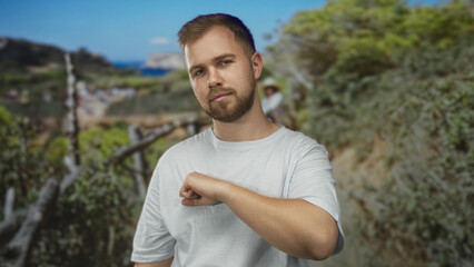 Young man with beard wearing white t shirt and fist extended toward camera in forest path; determination grit resilience.