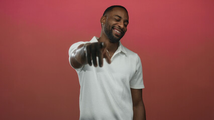 Man smiling and pointing finger at camera in studio against pink backdrop wearing white polo; confidence connection growth.