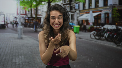 Woman in red tank top laughing and pointing finger on vibrant bustling cobblestone street at camera; joy.