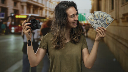 Smiling young hispanic woman fans cash and holds camera on busy downtown city street; optimism...