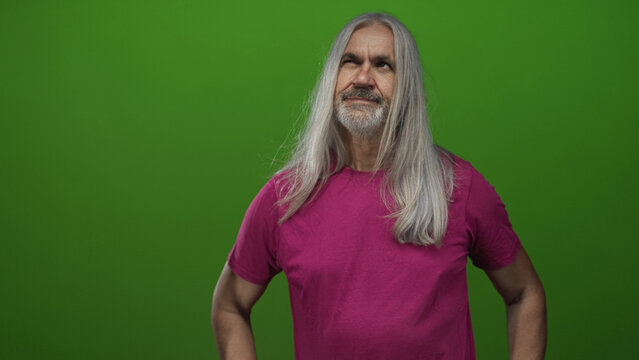 Man with long gray hair and beard posing with hand on chin in studio wearing magenta t shirt and bracelets, looking upward with pensive gaze; thoughtful reflection.