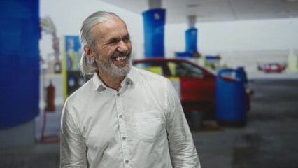 Man laughing with head thrown back at petrol station forecourt near fuel pump and car, wearing white shirt  carefree happiness. © Krakenimages.com