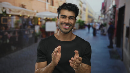 Naklejka premium Man wearing black shirt and silver bracelet claps hands while smiling on street during a sunny afternoon; celebration.