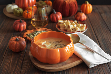 Creamy pumpkin soup with croutons and seeds, served in a pumpkin-shaped bowl on dark wooden table.