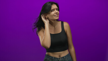 Woman holds hand to ear listening attentively on purple studio set with focused gaze and visible...