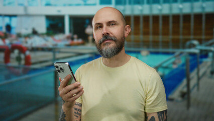 Man using smartphone on cruise ship with pool in background, enjoying seaside vacation outdoors during sunny day, showcasing technology and relaxation.