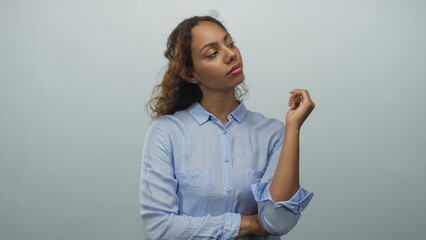 Woman with raised hand and folded arm posing in studio against pale blue wall; thoughtful...