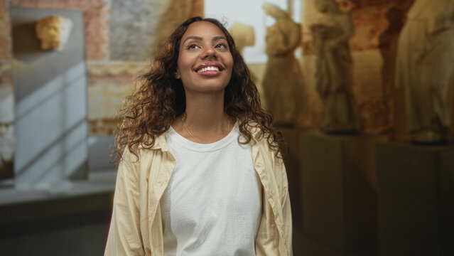 Woman smiling with face visible and eyes closed amid stone statues in the museum building; quiet joy.