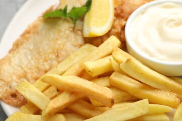 British Traditional Fish and chips with sauce, lemon and parsley on plate, closeup