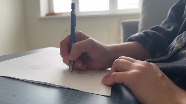 Close-up of a hand sketching on paper with a mechanical pencil. Natural daylight from a window, creative process, artistic workspace, concept of design and inspiration.