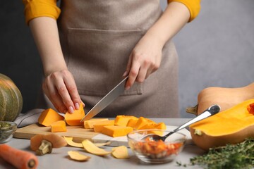 Woman cutting pumpkin at grey table, closeup