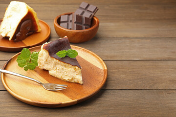 Pieces of delicious Basque cheesecake with mint and chocolate on wooden table, closeup. Space for text