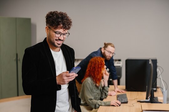 Professional man smiling, using smartphone at office