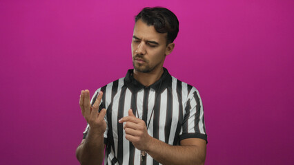 Young hispanic referee in striped shirt counting with fingers over pink background, focused and...