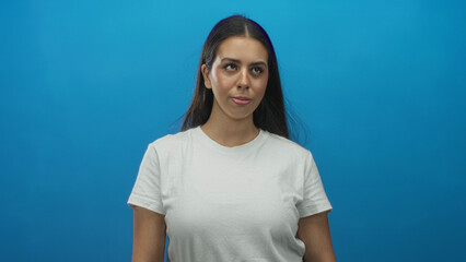 Woman young brunette with face visible, tongue out and eyes looking upward in studio blue backdrop; playful curiosity.