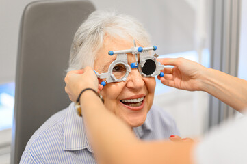 Cropped hands of female ophthalmologist using phoropter to test eyes of smiling senior patient during hospital visit
