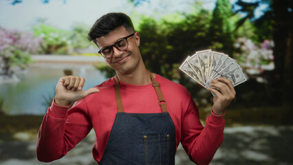 Man in outdoor park holding american dollar banknotes, smiling confidently wearing glasses and red...