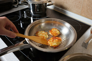 A man is frying potato pancakes in a steel pan in his home kitchen.